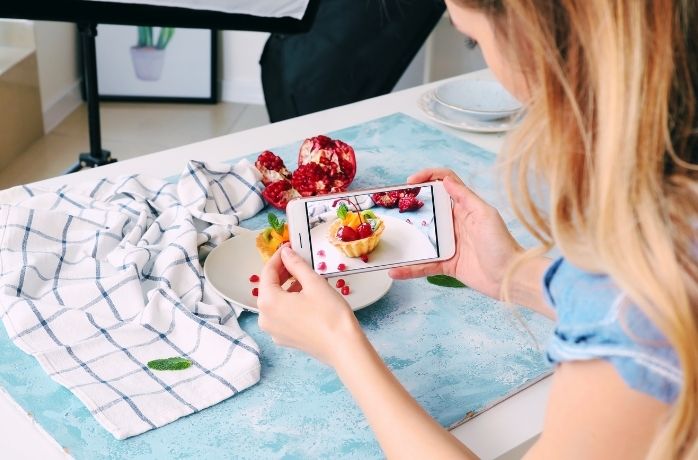 Female social media influencer with Mobile Phone Taking Picture of food on the table