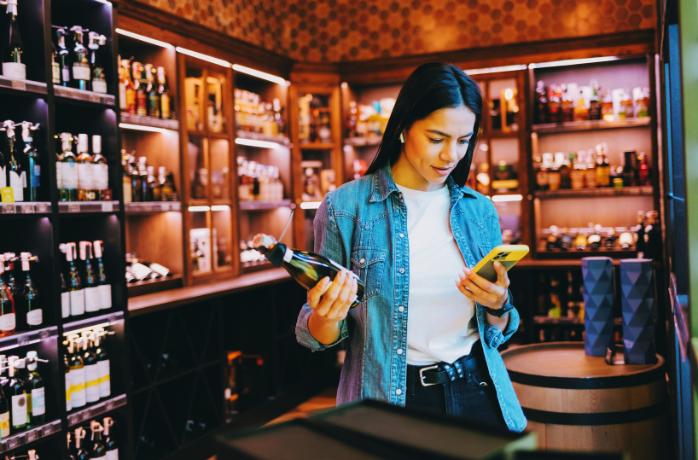 Woman with Phone Choosing wine in the Store