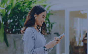 woman walking typing her phone with wired headphones on